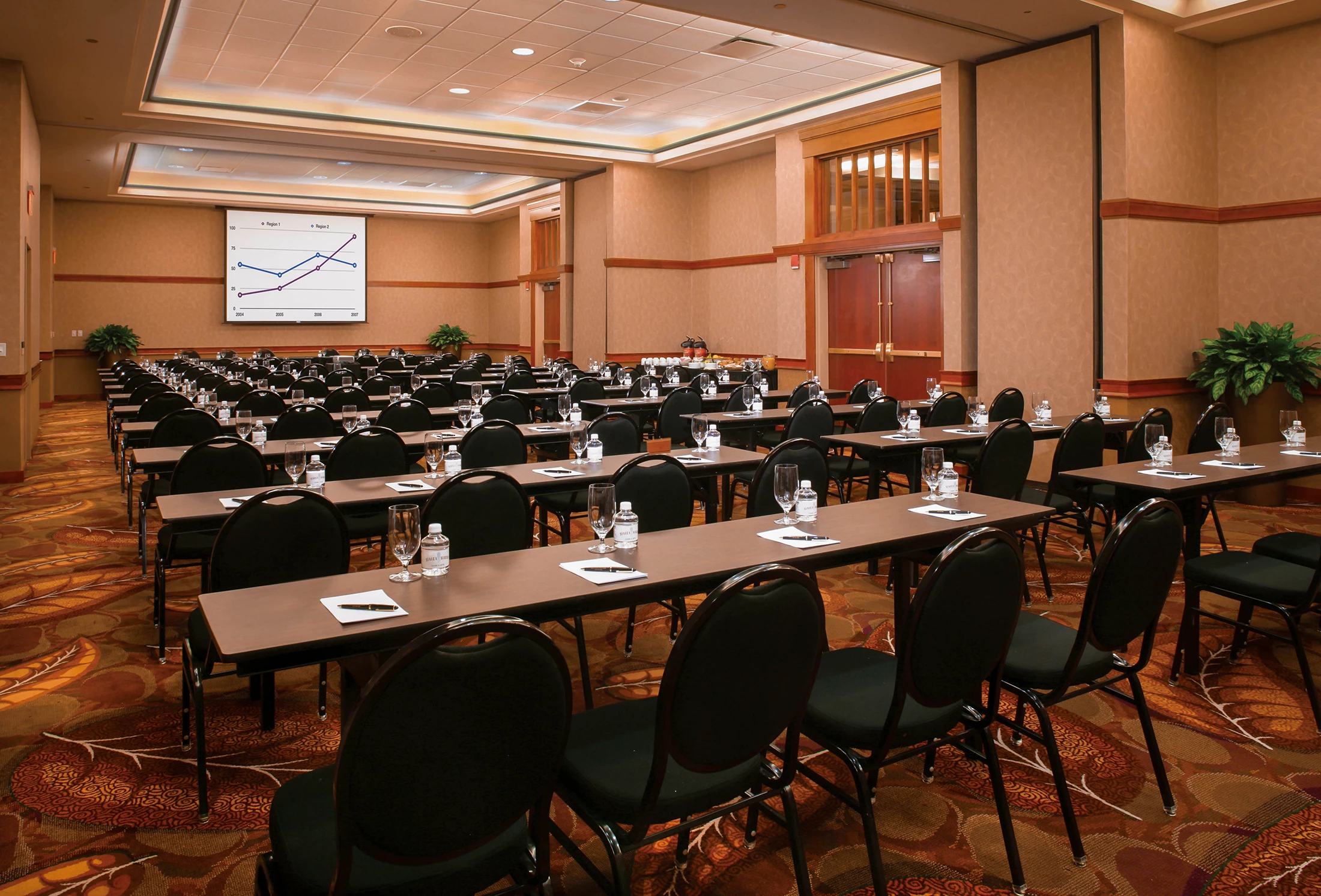 Meeting room set up with a projector screen and rows of tables and chairs facing the front.