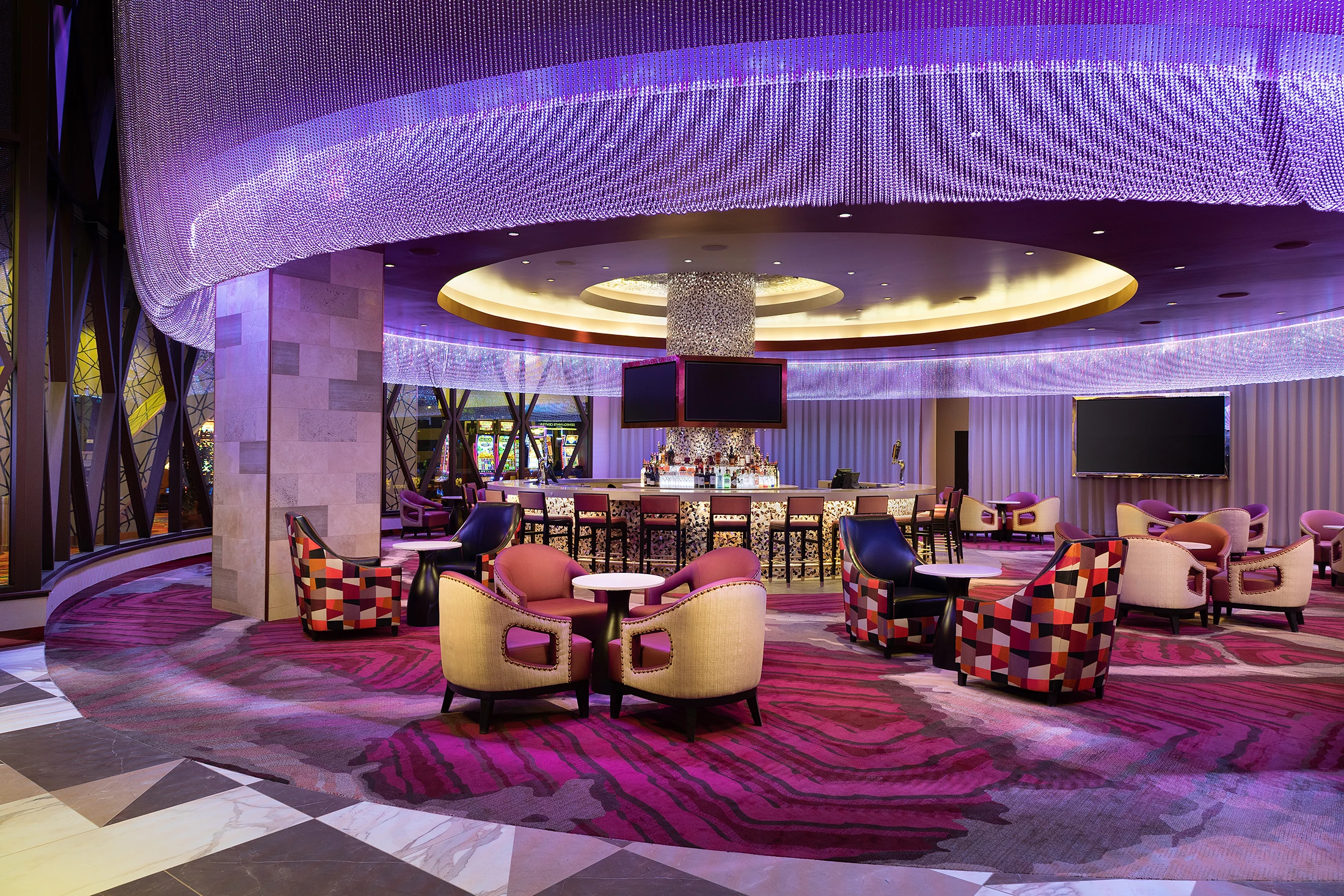 A lobby lounge with purple lighting and lounge chairs around tables.